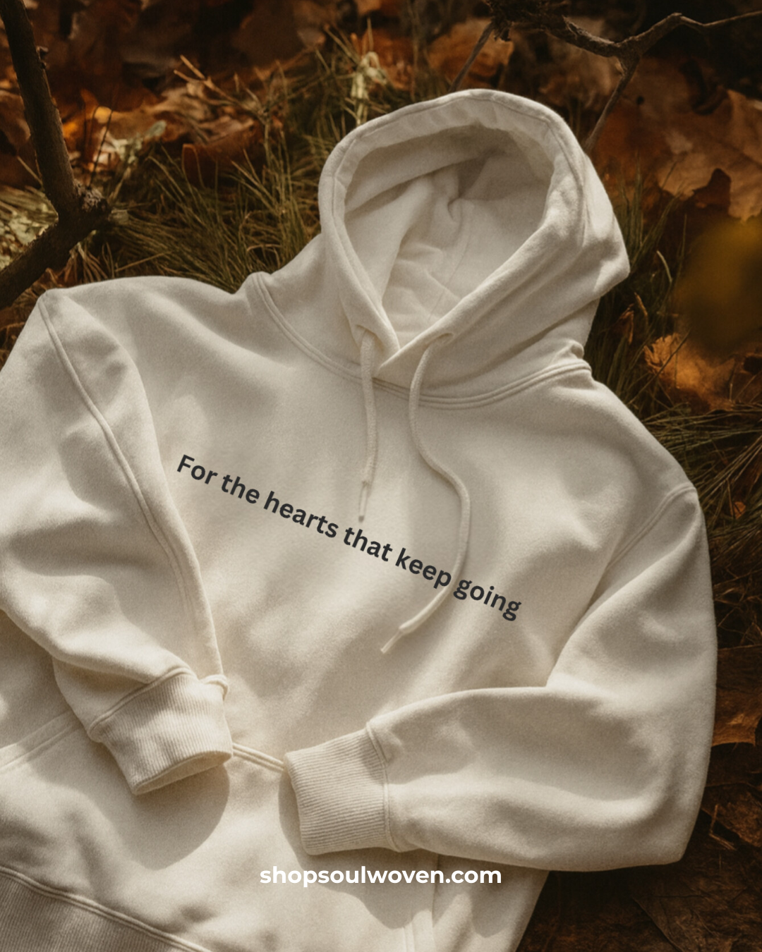 White hoodie with text 'For the hearts that keep going' on a natural background